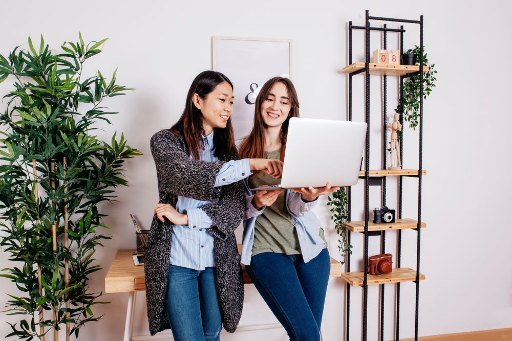 Two Asian business women smiling and whilst looking at laptop